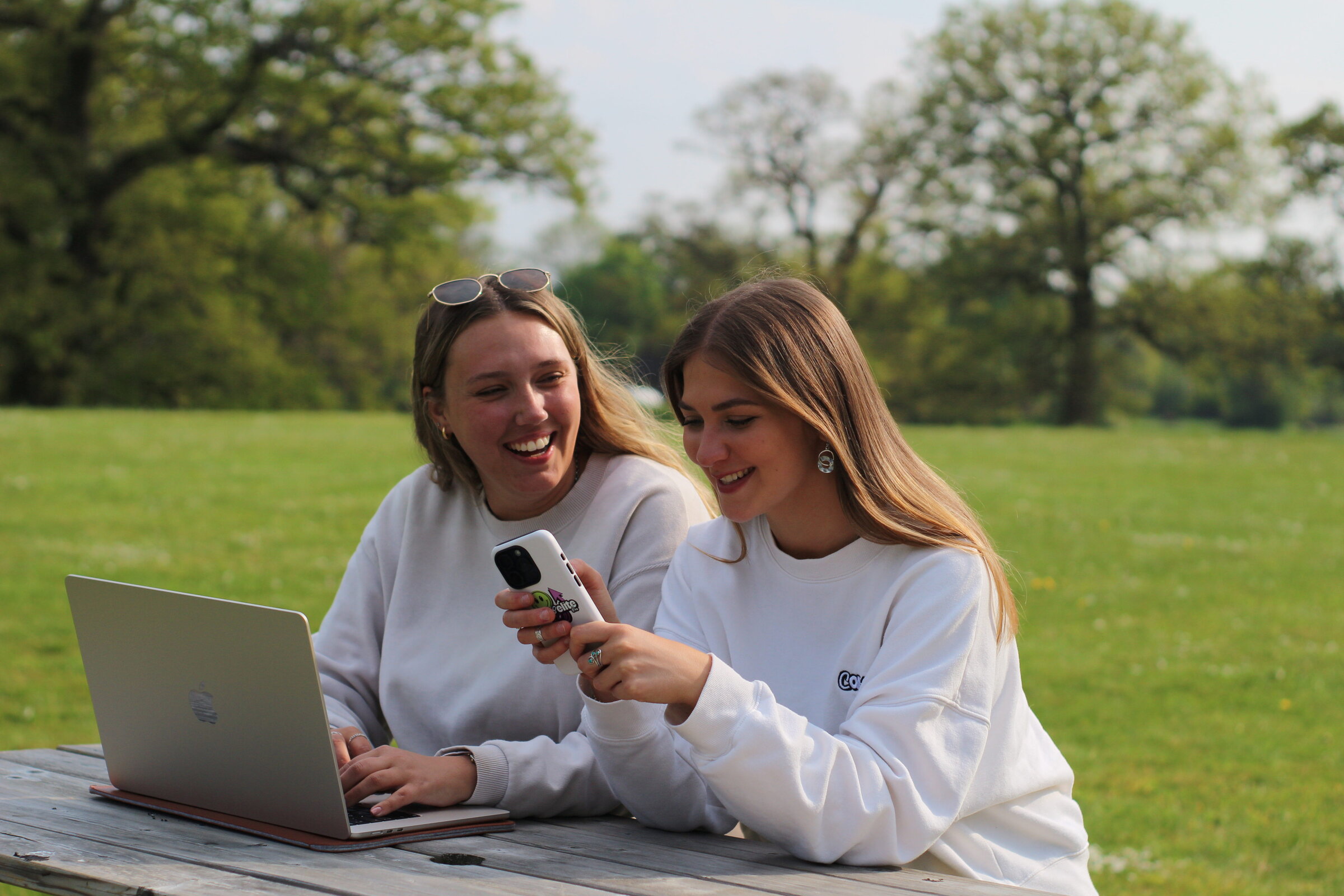 Two Compelite Pro team members laughing together at a picnic table with a laptop and phone — Bristol team culture
